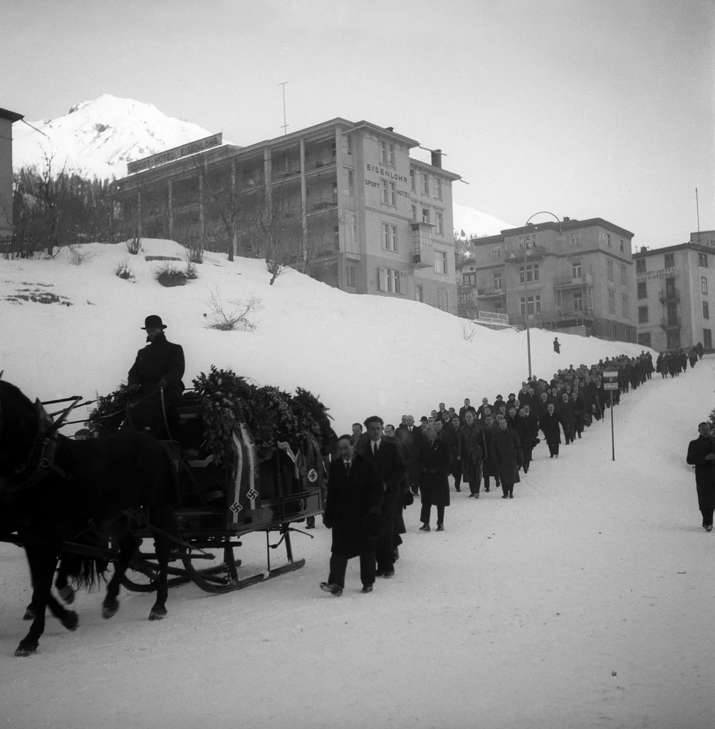 Auf seinem Sarg liegen Kränze von Adolf Hitler und Hermann Göring. Und hinter dem Sarg marschieren einige Dutzend schweizerische und deutsche Nazis. Im Sarg selbst liegt Wilhelm Gustloff, Landesgruppenleiter der NSDAP. Der deutsche Nazi-Chef in der Schweiz galt als antisemitischer und antidemokratischer Hardliner. Seine Aufgabe war es, die Schweiz auf eine Machtübernahme der Nazis vorzubereiten. Doch am Abend des 4. Februar 1936 wird Gustloff in seiner Davoser Wohnung mit vier Schüssen niedergestreckt. Tät…