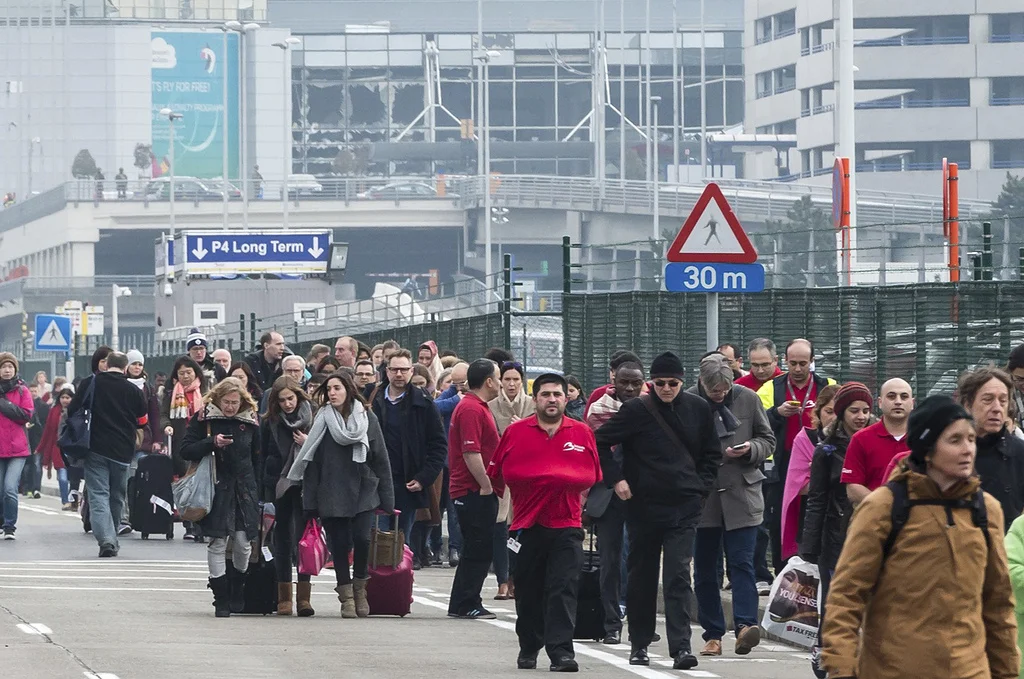 Passagiere und Angestellte verlassen zu Fuss den Flughafen Zaventem. Im Hintergrund die zertrümmerte Fensterfront der Abflughalle. (Foto: Keystone/AP/Geert Vanden Wijngaert)