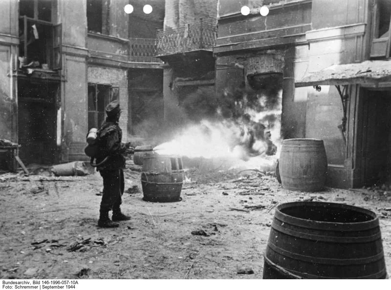 Das Bild stammt von der Propagandakompanie der Wehrmacht. In der Bildunterschrift hiess es: „Jedes Widerstandnest der Aufständischen muss einzeln ausgeräuchert werden. Die Strahlen eines deutschen Flammenwerfers vernichten hier jeden Widerstand, der aus einem schwer zugänglichen Kellerzugang immer wieder aufflackerte.“ (Bild: Deutsches Bundesarchiv, Bild 146-1996-057-10A, September 1944, Fotograf: Schremmer) 
 