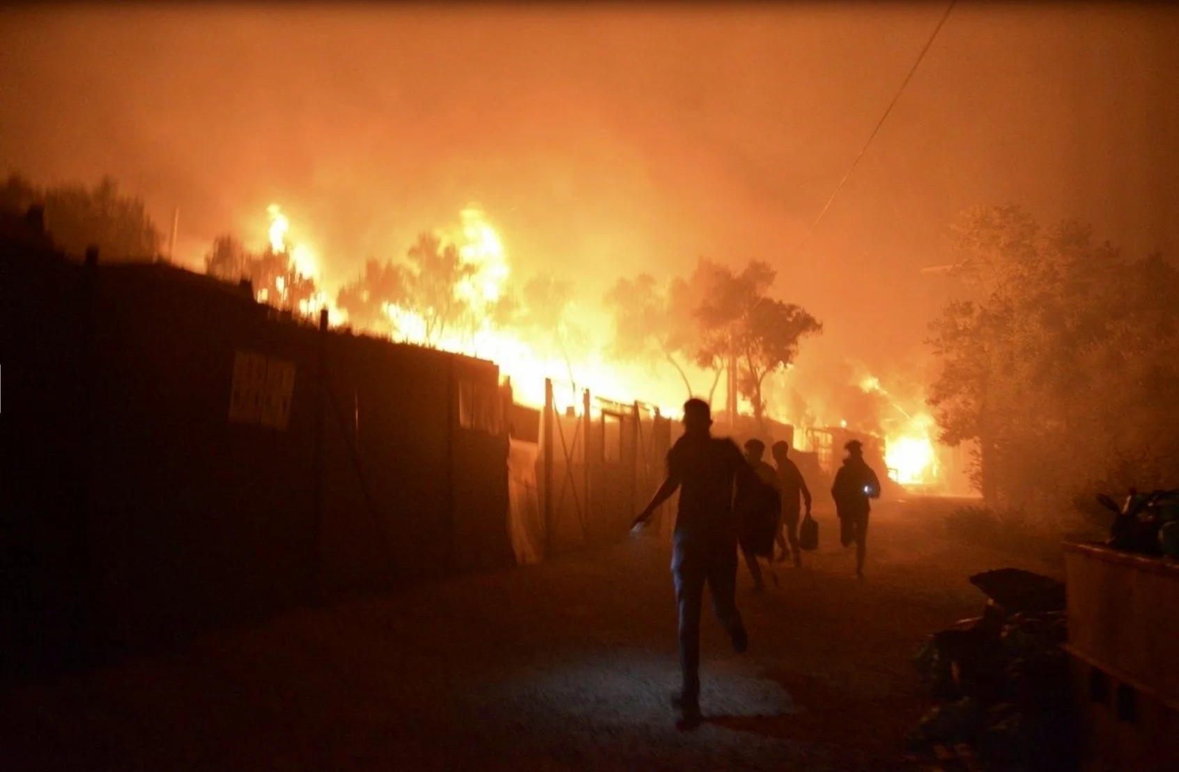 Flüchtlinge und Migranten fliehen im Lager Moria am frühen Morgen vor den in der Nacht ausgebrochenen Feuern. Das überbelegte griechische Aufnahmelager auf der Insel Lesbos in der nordöstlichen Ägäis unterliegt wegen Covid-19 einem Lockdown. Nachdem an mehreren Stellen Brände ausgebrochen sind, muss es jetzt trotzdem teilweise evakuiert werden. (Keystone/AP, Panagiotis Balaskas)