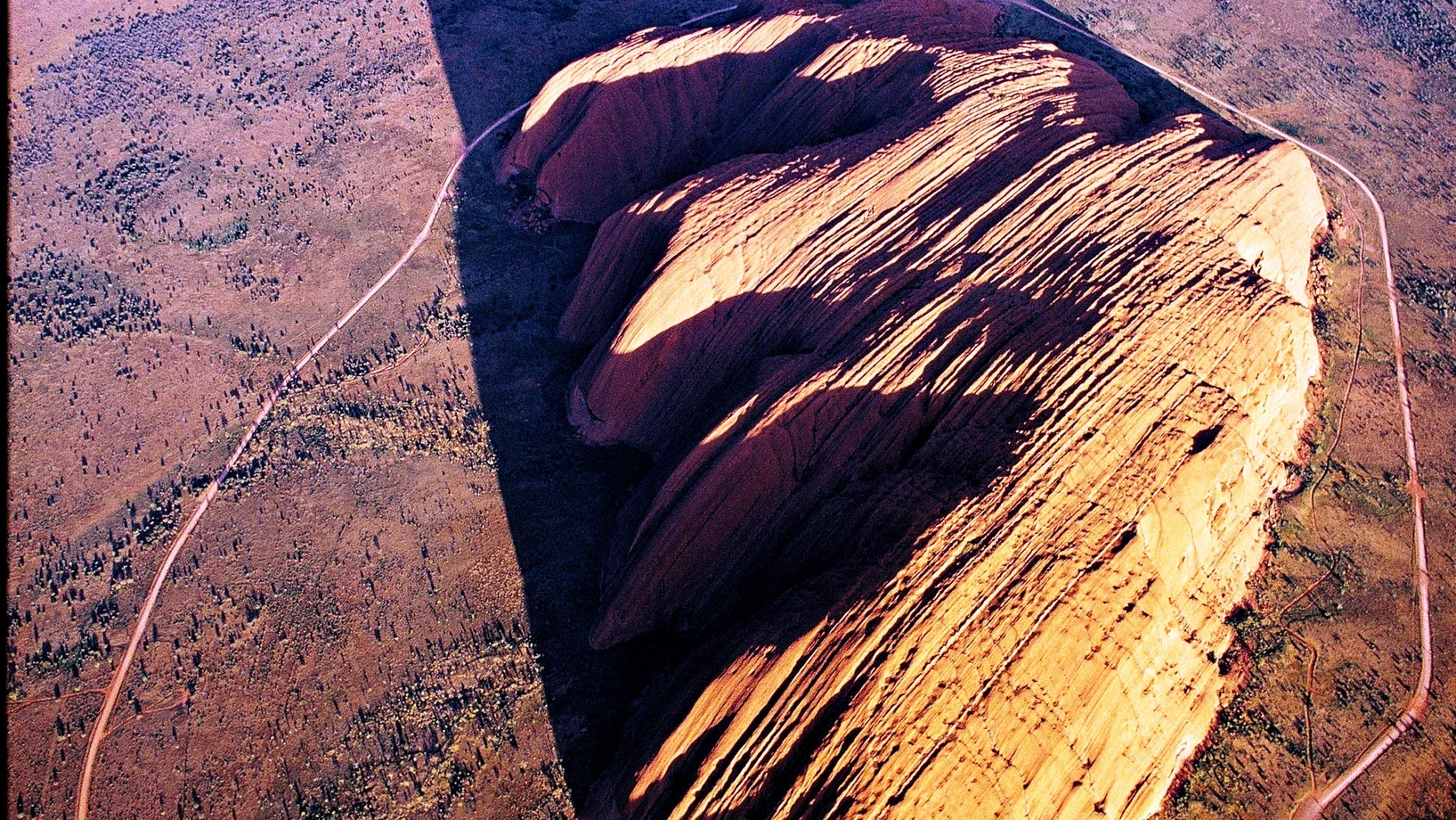Der Uluru, 348 Meter über die umgebende Wüste emporragend, ist ein Berg der dritten Art: ganz eingesponnen in die „Traumzeit“ der örtlichen Ureinwohner.
Mag ja sein, dass der Fels im roten toten Herzen Australiens schon kraft seiner Natur weltweit einzigartig ist – mitnichten ist er aber ein Monolith, obwohl sogar die Unesco dieses Touristenlatein nachplappert. Und als Inselberg aus geschichtetem Sandstein, den Erosion und Verwitterung aus einer Rumpffläche herauspräparierten, ist er nicht einmal – so ein…