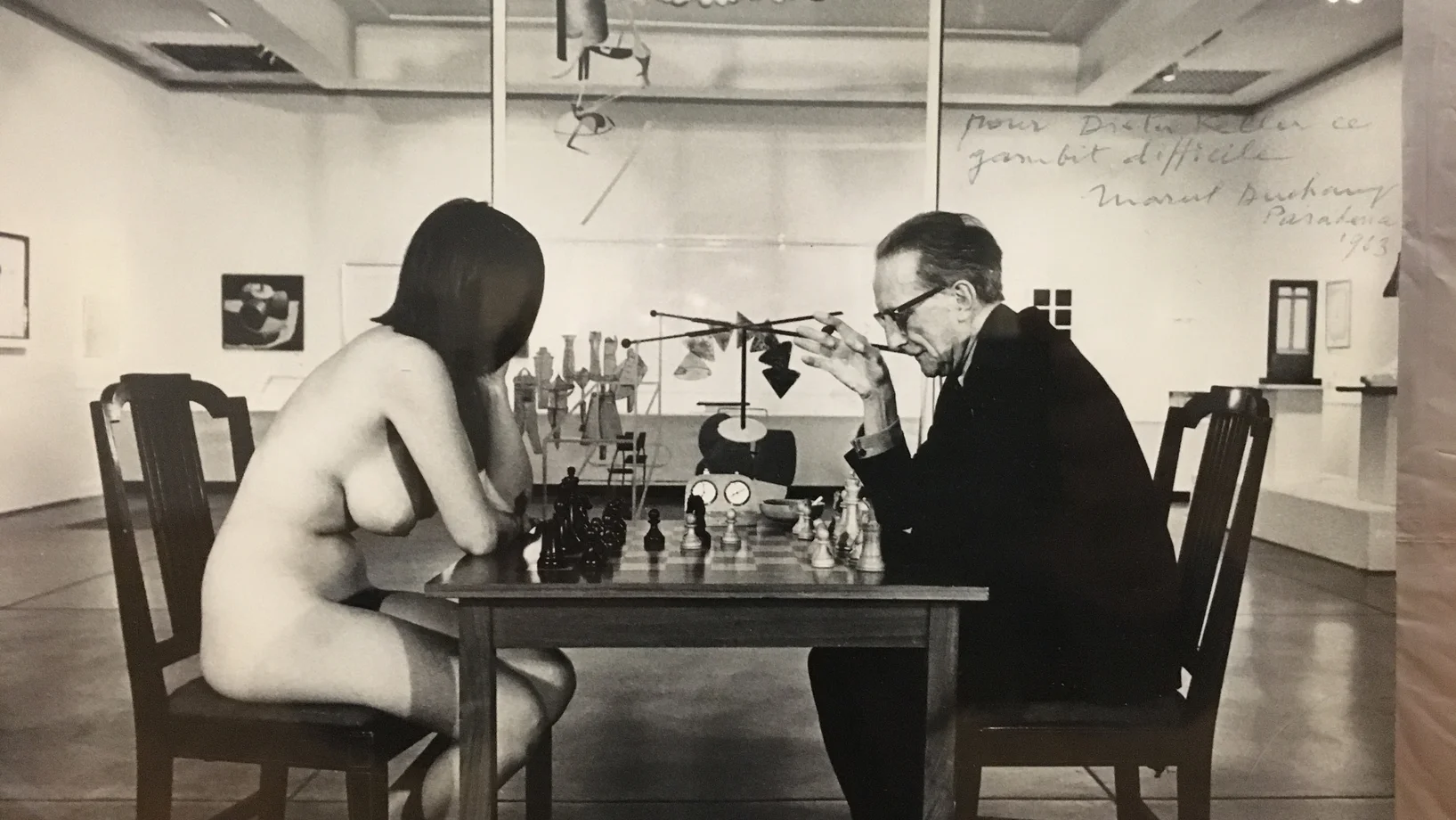 Duchamp war nicht nur ein Meister im Spiel mit der Kunst und der Selbstdarstellung, sondern auch ein Meister im Schachspiel. Das Foto von Julian Wasser zeigt ihn im Spiel gegen die 20jährige Künstlerin und Party-Gängerin Eve Babitz in der Duchamp-Retrospektive im Pasadena Art Museum 1963. Im Hintergrund das „Grosse Glas“.